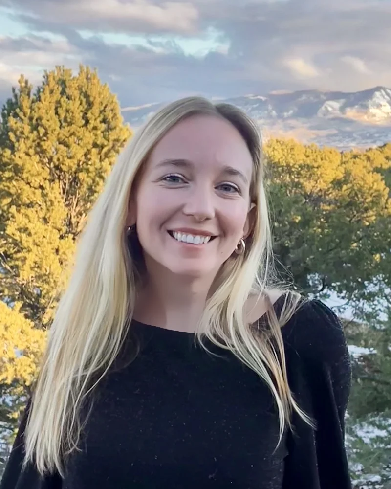 Madeline Sparks smiling outdoors with mountains and evergreen trees behind her